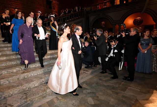 Crown Princess Victoria of Sweden (C) and Nobel Prize in Chemistry 2025 laureate Japanese chemist Susumu Kitagawa (R) arrive to attend the Nobel Prize banquet on December 10, 2025 at the City Hall in Stockholm, Sweden. The laureates received their prizes at formal ceremonies in Stockholm and Oslo on December 10. That date is the anniversary of the death in 1896 of scientist Alfred Nobel, who created the prizes in his will. (Photo by Jonathan Nackstrand / AFP)