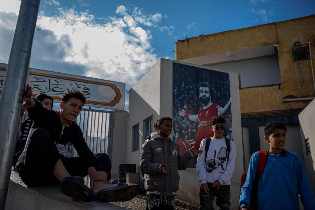 Footballers stand next a picture of Liverpool's footballer Mohamed Salah at his Youth Centre in the Egyptian village of Nagrig, about 120 kilometres northwest of Cairo on December 10, 2025. Salah, the Egypt international was omitted from the squad that travelled to Milan for a Champions League clash with Inter on December 9 following a blistering attack on manager Arne Slot and the club hierarchy after being left on the bench for last weekend's 3-3 draw at Leeds. (Photo by Khaled DESOUKI / AFP)