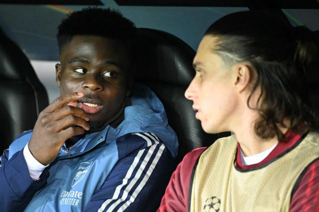 Arsenal's English forward #07 Bukayo Saka (L) talks with Arsenal's Italian defender #33 Riccardo Calafiori (R) on the bench during the UEFA Champions League, league phase - matchday 6, football match between Club Brugge and Arsenal at the Jan Breydel stadium in Bruges on December 10, 2025. (Photo by NICOLAS TUCAT / AFP)