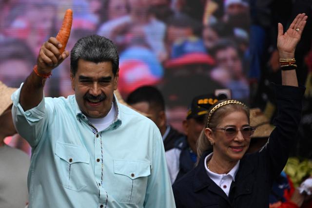 Venezuela's President Nicolas Maduro holds a carrot as he arrives with First Lady Cilia Flores at a rally marking the anniversary of the Battle of Santa Ines, in Caracas on December 10, 2025. (Photo by Federico PARRA / AFP)