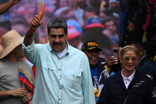 Venezuela's President Nicolas Maduro holds a carrot as he arrives with First Lady Cilia Flores at a rally marking the anniversary of the Battle of Santa Ines, in Caracas on December 10, 2025. (Photo by Federico PARRA / AFP)