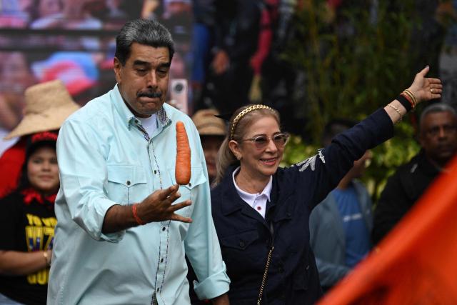 Venezuela's President Nicolas Maduro holds a carrot as he arrives with First Lady Cilia Flores at a rally marking the anniversary of the Battle of Santa Ines, in Caracas on December 10, 2025. (Photo by Federico PARRA / AFP)