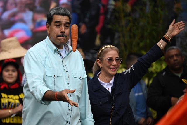 TOPSHOT - Venezuela's President Nicolas Maduro tosses a carrot into the air upon his arrival with First Lady Cilia Flores at a rally marking the anniversary of the Battle of Santa Ines, in Caracas on December 10, 2025. (Photo by Federico PARRA / AFP)