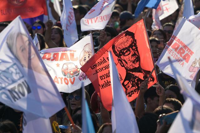 Supporters of Chile's presidential candidate Jeannette Jara, of the Unidad por Chile coalition, wave a flag depicting late Chile's President (1970-1973) Salvador Allende ahead of her closing campaign rally in Santiago on December 10, 2025. The second round of the Chilean presidential election on December 14 will pit two candidates against each other who are diametrically opposed: Jeannette Jara, the representative of a broad left-wing coalition with modest origins, and the far-right leader Jose Antonio Kast, an ultraconservative Catholic determined to massively expel undocumented migrants. (Photo by Rodrigo ARANGUA / AFP)
