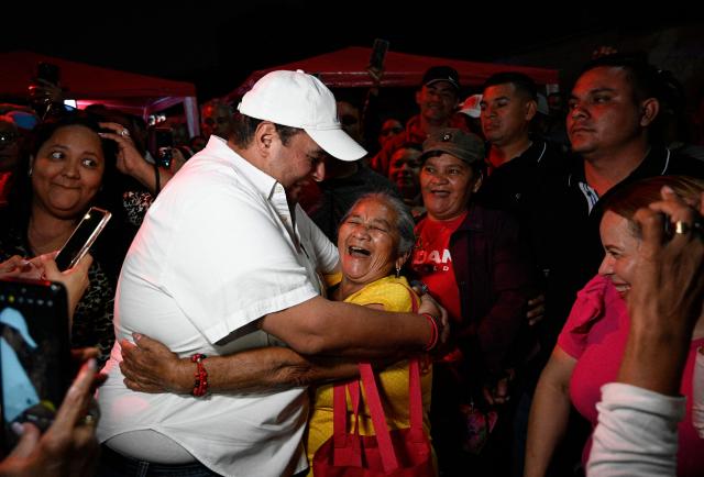Tegucigalpa's mayor and incumbent candidate Jorge Aldana dances with a ruling Libertad y Refundacion (LIBRE) party supporter at the Professional Formation National Institute headquarters, where the electoral material for last presidential election is being held, in Tegucigalpa on December 10, 2025. The Honduran military vowed on December 10, 2025, to ensure a peaceful transfer of power regardless of who wins a November 30 presidential election in which votes are still being counted amid interference claims. (Photo by Orlando SIERRA / AFP)