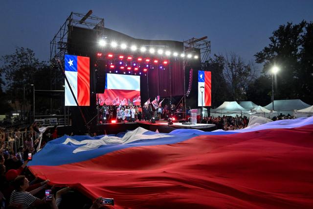 Supporters of Chile's presidential candidate Jeannette Jara of the Unidad por Chile coalition unfurl a giant Chilean flag during her closing campaign rally in Santiago on December 10, 2025. The second round of the Chilean presidential election on December 14 will pit two candidates against each other who are diametrically opposed: Jeannette Jara, the representative of a broad left-wing coalition with modest origins, and the far-right leader Jose Antonio Kast, an ultraconservative Catholic determined to massively expel undocumented migrants. (Photo by RODRIGO ARANGUA / AFP)