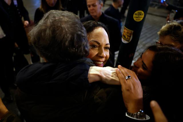 Nobel peace laureate Maria Corina Machado (C) is hugged by supporters gathered outside the Grand Hotel in Oslo, Norway, in the early hours of December 11, 2025. Machado arrived in Oslo hours after the Venezuelan opposition leader's award was collected on her behalf by her daughter. (Photo by Odd ANDERSEN / AFP)