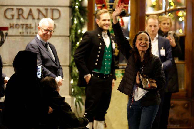 Nobel peace laureate Maria Corina Machado (R) waves to supporters gathered outside the Grand Hotel in Oslo, Norway, in the early hours of December 11, 2025. Machado arrived in Oslo hours after the Venezuelan opposition leader's award was collected on her behalf by her daughter. (Photo by Odd ANDERSEN / AFP)