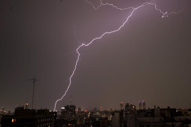 Lightning strikes buildings during a thunderstorm over Buenos Aires on December 11, 2025. (Photo by Luis ROBAYO / AFP)