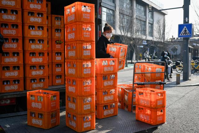 A worker loads drink cases onto a truck along a street in Beijing on December 11, 2025. (Photo by WANG Zhao / AFP)