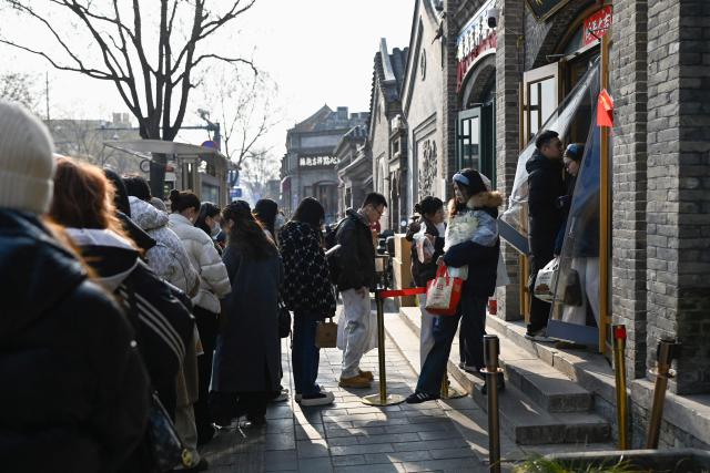 People queue up at the entrance of a cake shop in Beijing on December 11, 2025. (Photo by WANG Zhao / AFP)