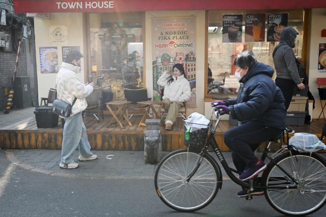 A couple take a picture in front of a Christmas poster outside a cafe in Beijing on December 11, 2025. (Photo by WANG Zhao / AFP)