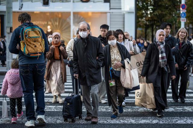 People cross a street in the Ginza area of Tokyo on December 11, 2025. (Photo by Yuichi YAMAZAKI / AFP)