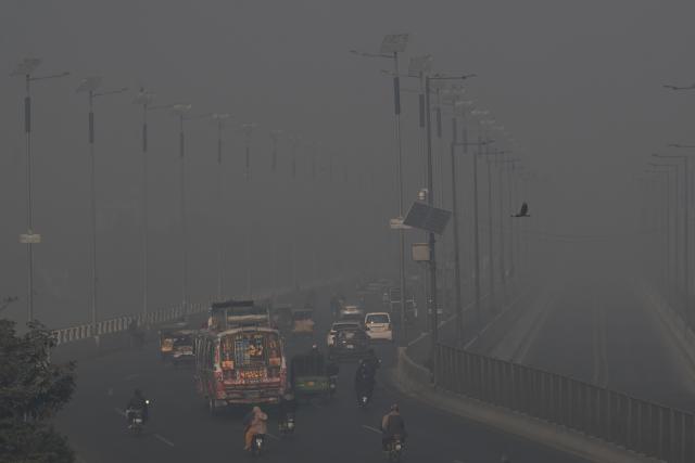Commuters drive along a road amid dense smog in Lahore on December 11, 2025. (Photo by Arif ALI / AFP)
