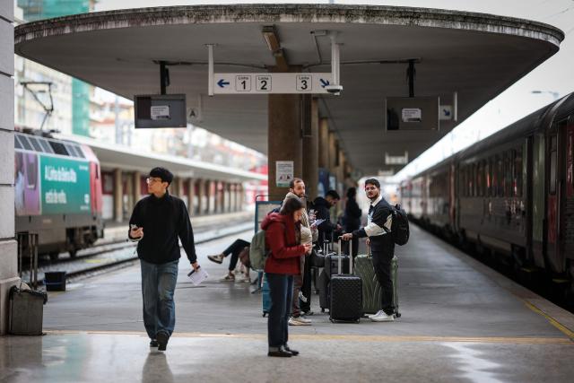 People stand on the platform waiting for trains to departure at Santa Apolonia train station during a general strike in Lisbon on December 11, 2025. Portugal braced on Thursday for its first general strike in 12 years, as unions urge action against the right-wing minority government's planned workers' rights reforms. Widespread disruption is expected for public transport, schools, courts and hospitals, as workers protest against a draft law aiming to simplify firing procedures, extend the length of fixed-term contracts and expand the minimum services required during a strike. (Photo by PATRICIA DE MELO MOREIRA / AFP)