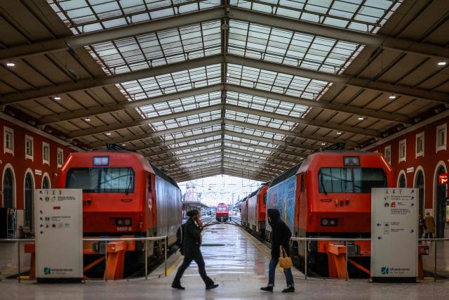 People walk  on a platform in front of idle trains at Santa Apolonia train station during a general strike in Lisbon on December 11, 2025. Portugal braced on Thursday for its first general strike in 12 years, as unions urge action against the right-wing minority government's planned workers' rights reforms. Widespread disruption is expected for public transport, schools, courts and hospitals, as workers protest against a draft law aiming to simplify firing procedures, extend the length of fixed-term contracts and expand the minimum services required during a strike. (Photo by PATRICIA DE MELO MOREIRA / AFP)