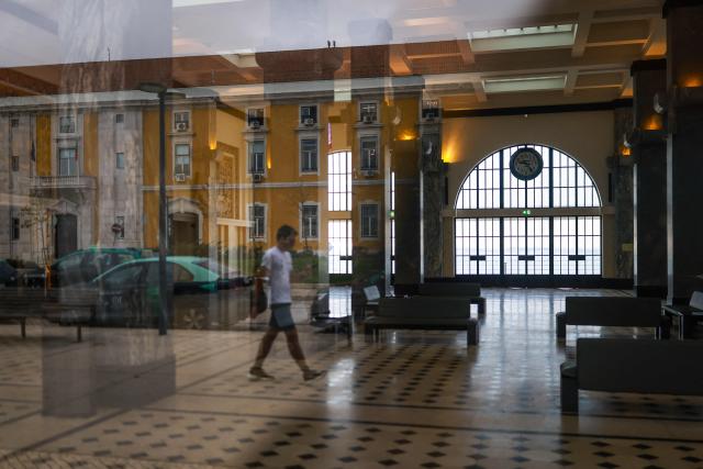 A pedestrian is reflected in the window of an empty Terreiro do Paco boat station which was closed during a general strike in Lisbon on December 11, 2025. Portugal braced on Thursday for its first general strike in 12 years, as unions urge action against the right-wing minority government's planned workers' rights reforms. Widespread disruption is expected for public transport, schools, courts and hospitals, as workers protest against a draft law aiming to simplify firing procedures, extend the length of fixed-term contracts and expand the minimum services required during a strike. (Photo by PATRICIA DE MELO MOREIRA / AFP)