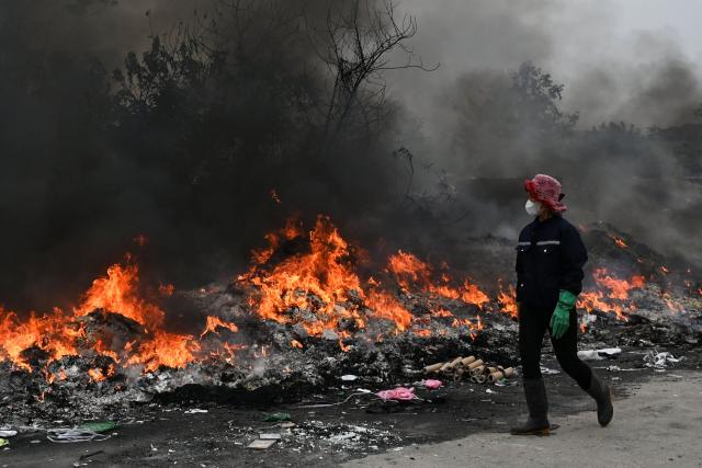 A woman looking for items in the trash to salvage walks past a burning pile of garbage on the roadside in Hanoi on December 11, 2025. Toxic smog has blanketed Vietnam's capital for more than a week, blotting out the skyline and leaving residents wheezing as Hanoi's air quality dipped to among the world's worst on December 11. (Photo by Nhac NGUYEN / AFP)