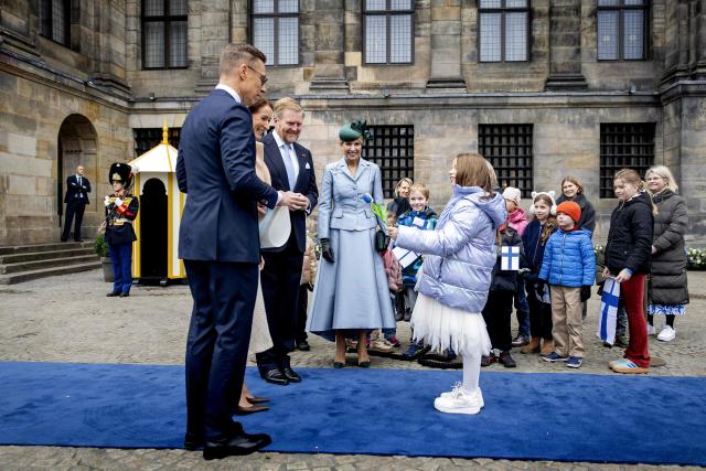A child offers a tulip during a welcome ceremony with Netherlands' King Willem-Alexander (3rd-R) and Netherland's Queen Máxima (C), Finland's President Alexander Stubb (L) and his wife Suzanne Innes-Stubb (2nd-L) on Dam Square on the first day of a two-day state visit to the Netherlands, in Amsterdam on December 11, 2025. (Photo by Koen van Weel / ANP / AFP) / Netherlands OUT