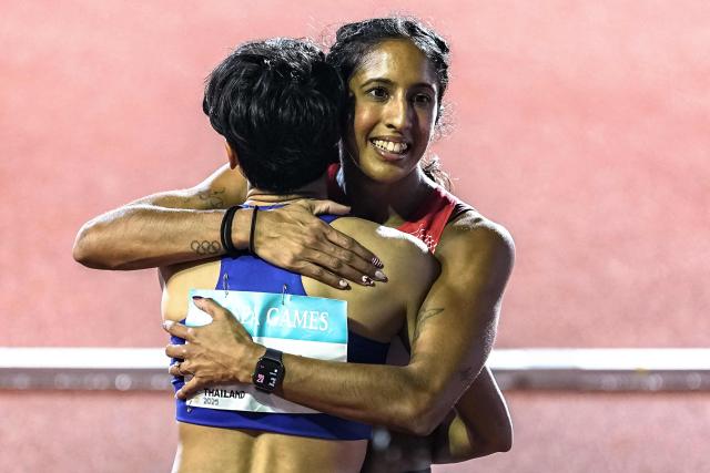 Singapore's Shanti Pereira (R) hugs Thailand's Supanich Poolkerd after the women's 100m final of the athletics event during the 33rd Southeast Asian Games (SEA Games) at the Suphachalasai National Stadium in Bangkok on December 11, 2025. (Photo by Chanakarn Laosarakham / AFP)