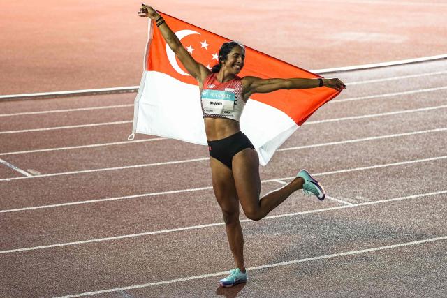 Singapore's Shanti Pereira celebrates with the Singapore national flag after winning the women's 100m final of the athletics event during the 33rd Southeast Asian Games (SEA Games) at the Suphachalasai National Stadium in Bangkok on December 11, 2025. (Photo by Chanakarn Laosarakham / AFP)