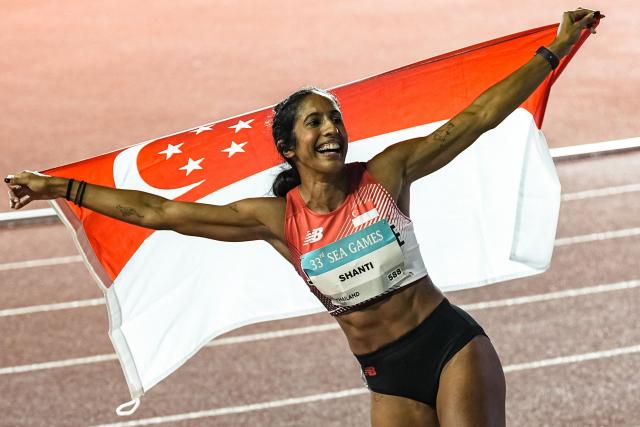 Singapore's Shanti Pereira celebrates with the Singapore national flag after winning the women's 100m final of the athletics event during the 33rd Southeast Asian Games (SEA Games) at the Suphachalasai National Stadium in Bangkok on December 11, 2025. (Photo by Chanakarn Laosarakham / AFP)