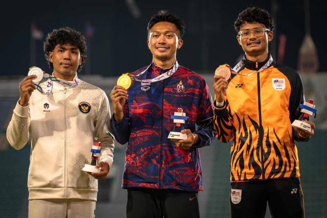 Thailand's Puripol Boonson (C) poses for photos with his gold medal next to silver medalist Indonesia's Lalu Muhammad Zohri (L) and bronze medalist Malaysia's Danish Iftikhar Muhammad Roslee after the men's 100m final of the athletics event during the 33rd Southeast Asian Games (SEA Games) at the Suphachalasai National Stadium in Bangkok on December 11, 2025. (Photo by Chanakarn Laosarakham / AFP)