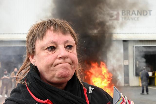 An employee reacts holding binders next to a fire at the Brandt factory, in Vendome, central France on December 11, 2025 following the verdict of the court. On December 11, 2025, the court ordered the liquidation of the century-old home-appliance group Brandt, a flagship of French industry that has been in serious trouble since it was placed under court-supervised restructuring, the president of the Centre-Val de Loire region told AFP. (Photo by JEAN-FRANCOIS MONIER / AFP)