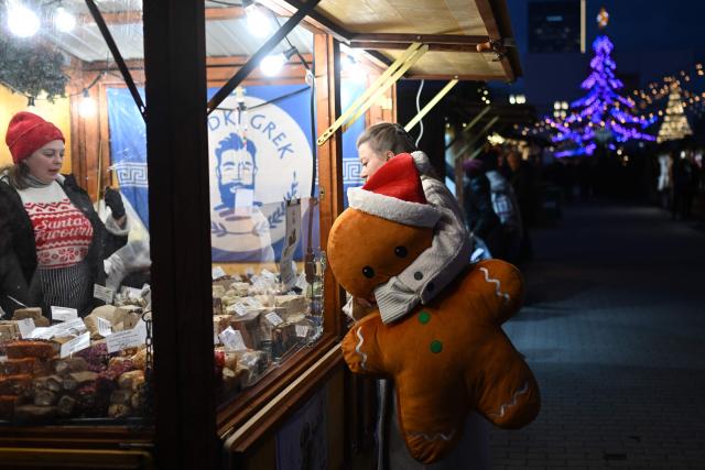 A woman holds a giant gingerbread man stuffed-toy as she visits the Christmas market in central Warsaw on December 11, 2025. (Photo by Sergei GAPON / AFP)