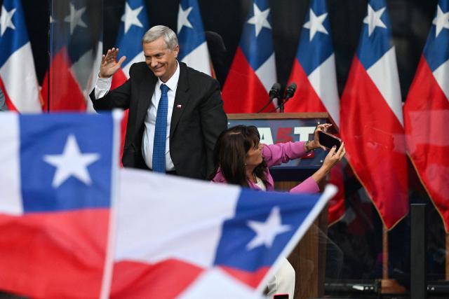 Chile's presidential candidate Jose Antonio Kast of the Republican Party waves to supporters as his wife Maria Adriasola takes a photo during his closing campaign rally in Temuco, Chile on December 11, 2025. The second round of the Chilean presidential election on December 14 will pit two candidates against each other who are diametrically opposed: Jeannette Jara, the representative of a broad left-wing coalition with modest origins, and the far-right leader Jose Antonio Kast, an ultraconservative Catholic determined to massively expel undocumented migrants. (Photo by Eitan ABRAMOVICH / AFP)