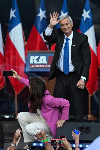 Chile's presidential candidate Jose Antonio Kast of the Republican Party waves to supporters as his wife Maria Adriasola takes a photo during his closing campaign rally in Temuco, Chile on December 11, 2025. The second round of the Chilean presidential election on December 14 will pit two candidates against each other who are diametrically opposed: Jeannette Jara, the representative of a broad left-wing coalition with modest origins, and the far-right leader Jose Antonio Kast, an ultraconservative Catholic determined to massively expel undocumented migrants. (Photo by Eitan ABRAMOVICH / AFP)