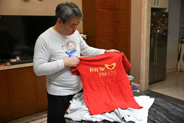 In this picture taken on December 10, 2025, Jiang Hui, whose mother was on board the missing Malaysia Airlines flight MH370, is seen showing items commemorating the accident at his home in Beijing. When Jiang Hui thinks of his mother, he remembers her waving goodbye as she left for her Malaysia Airlines flight, a bag slung across her shoulder and promising to return with souvenirs from her trip. Jiang Cuiyun, then a 72-year-old retiree, was one of 239 people aboard flight MH370 when it vanished from radar screens on March 8, 2014, en route from Kuala Lumpur to Beijing. (Photo by Pedro PARDO / AFP) / TO GO WITH AFP STORY:  China-Malaysia-aviation-accident, by Isabel Kua