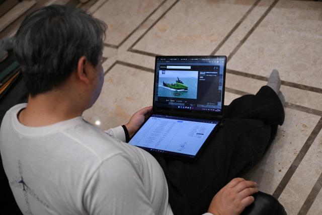 In this picture taken on December 10, 2025, Jiang Hui, whose mother was on board the missing Malaysia Airlines flight MH370, is seen showing a picture of the search for the plane at his home in Beijing. When Jiang Hui thinks of his mother, he remembers her waving goodbye as she left for her Malaysia Airlines flight, a bag slung across her shoulder and promising to return with souvenirs from her trip. Jiang Cuiyun, then a 72-year-old retiree, was one of 239 people aboard flight MH370 when it vanished from radar screens on March 8, 2014, en route from Kuala Lumpur to Beijing. (Photo by Pedro PARDO / AFP) / TO GO WITH AFP STORY:  China-Malaysia-aviation-accident, by Isabel Kua