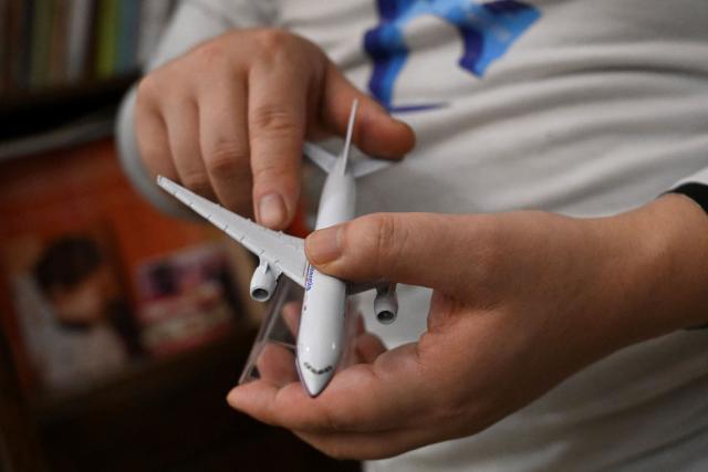In this picture taken on December 10, 2025, Jiang Hui, whose mother was on board the missing Malaysia Airlines flight MH370, is seen holding a miniature model of a Malaysia Airlines Boeing 777 aircraft at his home in Beijing. When Jiang Hui thinks of his mother, he remembers her waving goodbye as she left for her Malaysia Airlines flight, a bag slung across her shoulder and promising to return with souvenirs from her trip. Jiang Cuiyun, then a 72-year-old retiree, was one of 239 people aboard flight MH370 when it vanished from radar screens on March 8, 2014, en route from Kuala Lumpur to Beijing. (Photo by Pedro PARDO / AFP) / TO GO WITH AFP STORY:  China-Malaysia-aviation-accident, by Isabel Kua