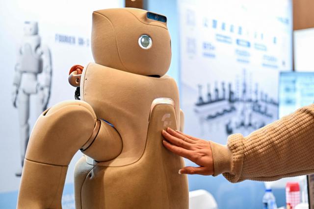 A man touches to a Fourier GR-3 humanoid robot by Fourier-Robotics at the Global Developer Pioneers Summit in Shanghai on December 12, 2025. (Photo by Hector RETAMAL / AFP)