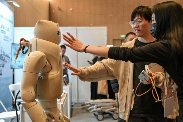 People touch to a Fourier GR-3 humanoid robot by Fourier-Robotics at the Global Developer Pioneers Summit in Shanghai on December 12, 2025. (Photo by Hector RETAMAL / AFP)