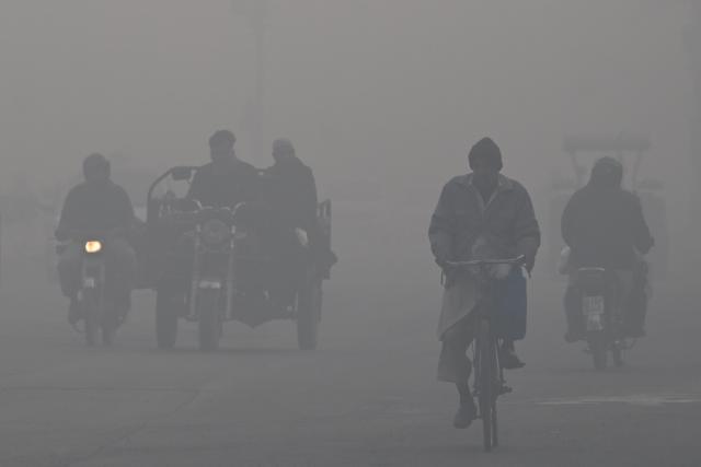 Commuters ride along a road amid dense smog in Lahore on December 12, 2025. (Photo by ARIF ALI / AFP)
