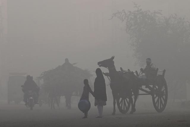 Commuters ride along a road amid dense smog in Lahore on December 12, 2025. (Photo by ARIF ALI / AFP)