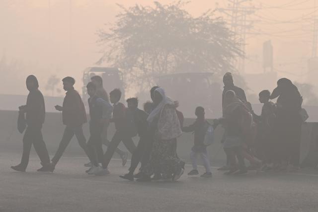 People walk across a road amid dense smog in Lahore on December 12, 2025. (Photo by ARIF ALI / AFP)