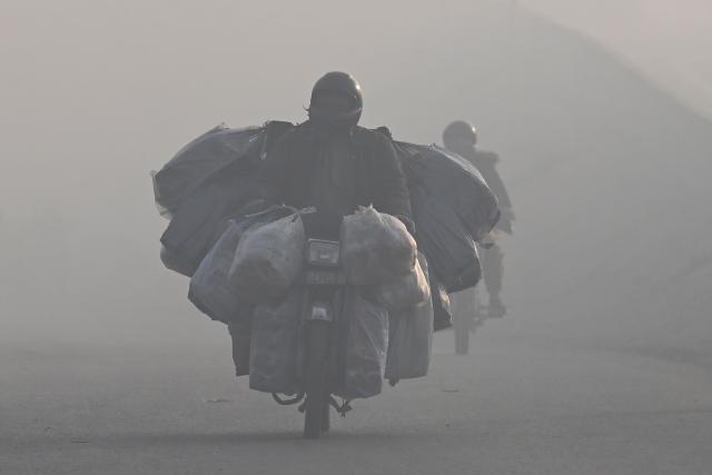 Commuters ride along a road amid dense smog in Lahore on December 12, 2025. (Photo by ARIF ALI / AFP)