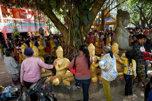 Displaced residents gather next to statues to receive aid at a temporary camp set up in a pagoda in Cambodia's Siem Reap province on December 12, 2025, amid clashes along the Cambodia-Thailand border.  (Photo by TANG CHHIN Sothy / AFP)