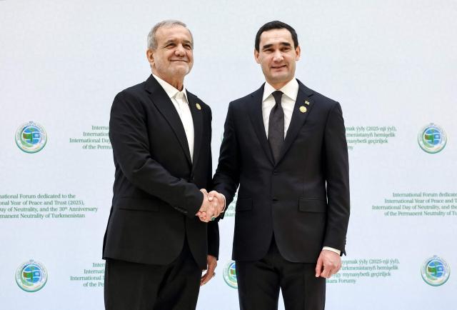 In this pool photograph distributed by the Russian state agency Sputnik, Turkmen President Serdar Berdymukhamedov welcomes Iranian President Masoud Pezeshkian during an international forum dedicated to the 30th anniversary of Turkmenistan's "permanent neutrality" status in Ashgabat on December 12, 2025. (Photo by Alexander KAZAKOV / POOL / AFP)