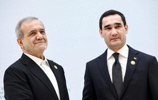 In this pool photograph distributed by the Russian state agency Sputnik, Turkmen President Serdar Berdymukhamedov welcomes Iranian President Masoud Pezeshkian during an international forum dedicated to the 30th anniversary of Turkmenistan's "permanent neutrality" status in Ashgabat on December 12, 2025. (Photo by Alexander KAZAKOV / POOL / AFP)