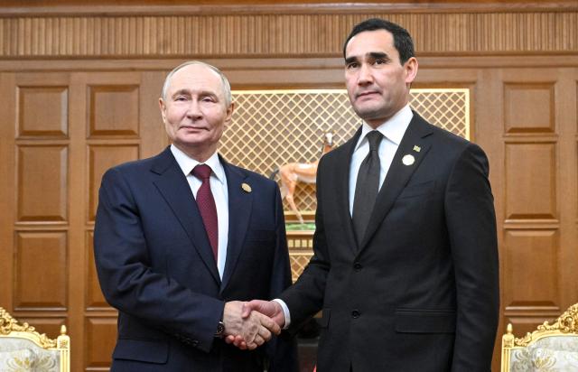 In this pool photograph distributed by the Russian state agency Sputnik, Russia's President Vladimir Putin and Turkmen President Serdar Berdymukhamedov hold a meeting in Ashgabat on December 12, 2025. (Photo by Kristina Kormilitsyna / POOL / AFP)