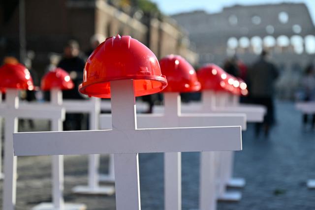 An installation of white crosses with red helmets recall deaths at work at the Imperial Forum avenue in Rome during a national day of strike by Italian union "Confederazione Generale Italiana del Lavoro" (CGIL) against the government's budget law, on December 12, 2025. (Photo by Alberto PIZZOLI / AFP)