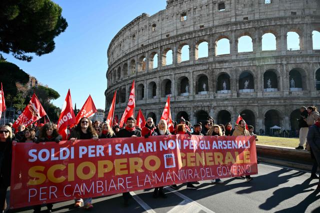 People march behind a banner reading "Money for salaries - not for armaments" near the Colosseum during a national day of strike by Italian union "Confederazione Generale Italiana del Lavoro" (CGIL) against the government's budget law, on December 12, 2025. (Photo by Alberto PIZZOLI / AFP)
