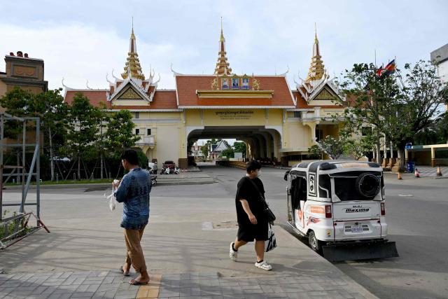 People walk near the closed Poipet International border checkpoint between Cambodia and Thailand in Poipet, Banteay Meanchey province on December 12, 2025, amid clashes along the Cambodia-Thailand border. (Photo by TANG CHHIN Sothy / AFP)