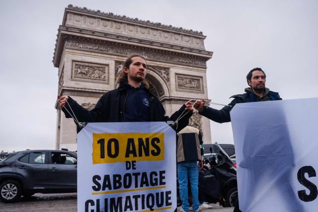 An activist holds a banner reading "10 years of climate sabotage" during a Greenpeace action in front of the Arc de Triomphe in Paris on December 12, 2025, marking the 10 year anniversary of the signing of the Paris Climate accords. (Photo by Dimitar DILKOFF / AFP)
