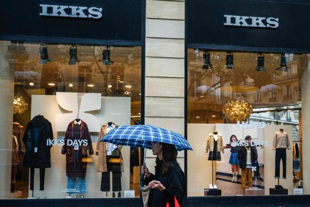 (FILES) A woman protects herself with an umbrella from the rain as she walks past a store of IKKS clothing brand in central Paris on October 3, 2025. The fashion group IKKS has been taken over, but around 500 out of 1,000 jobs are being cut, according to a court decision on December 12, 2025. (Photo by Dimitar DILKOFF / AFP)