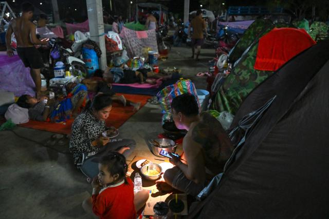A displaced family uses a flashlight as they eat a meal at a temporary camp in Banteay Meanchey province on December 12, 2025, amid clashes along the Cambodia-Thailand border. (Photo by TANG CHHIN Sothy / AFP)